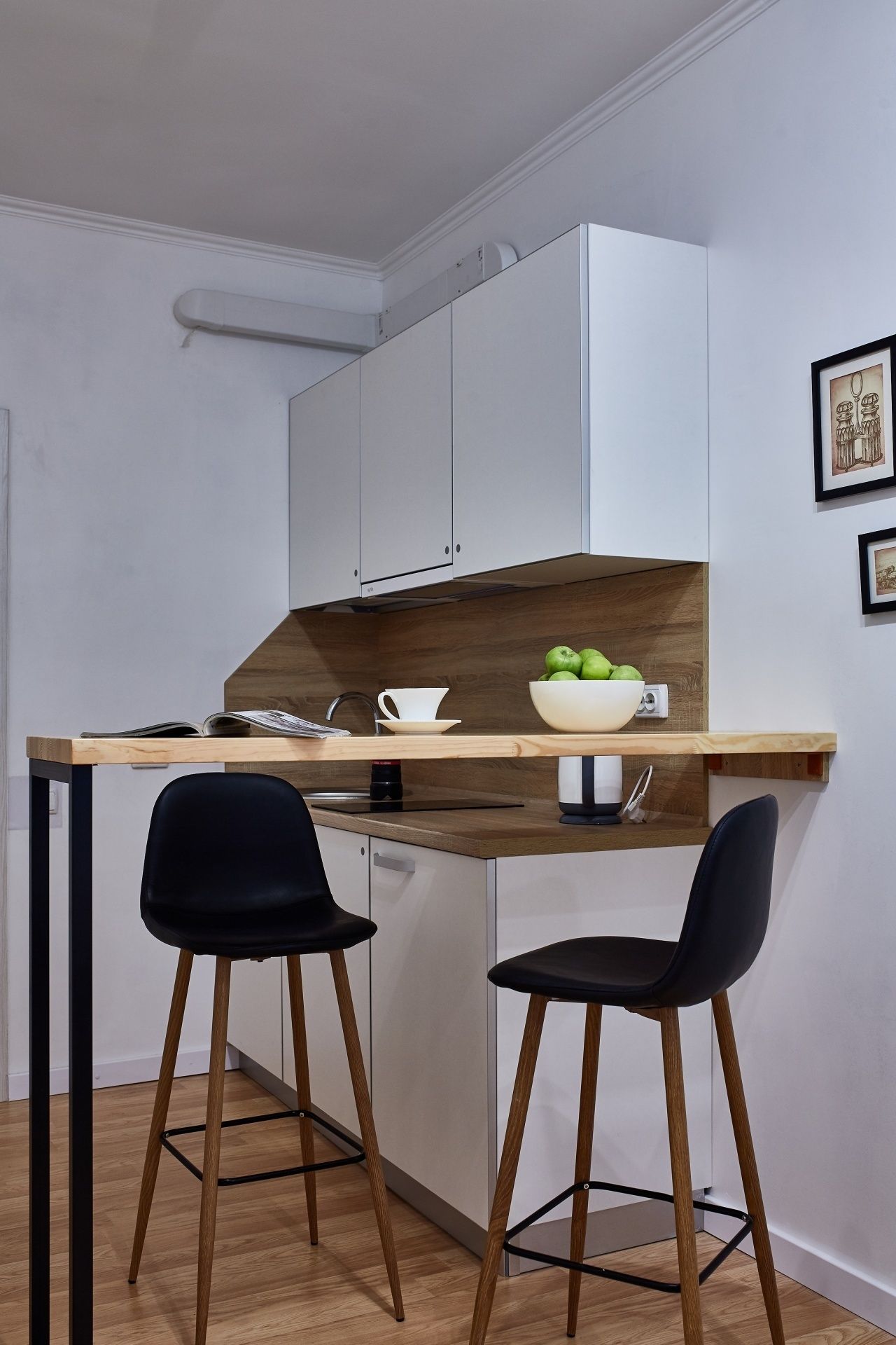 A compact kitchen with a wooden countertop, two black chairs, and a white cabinet.