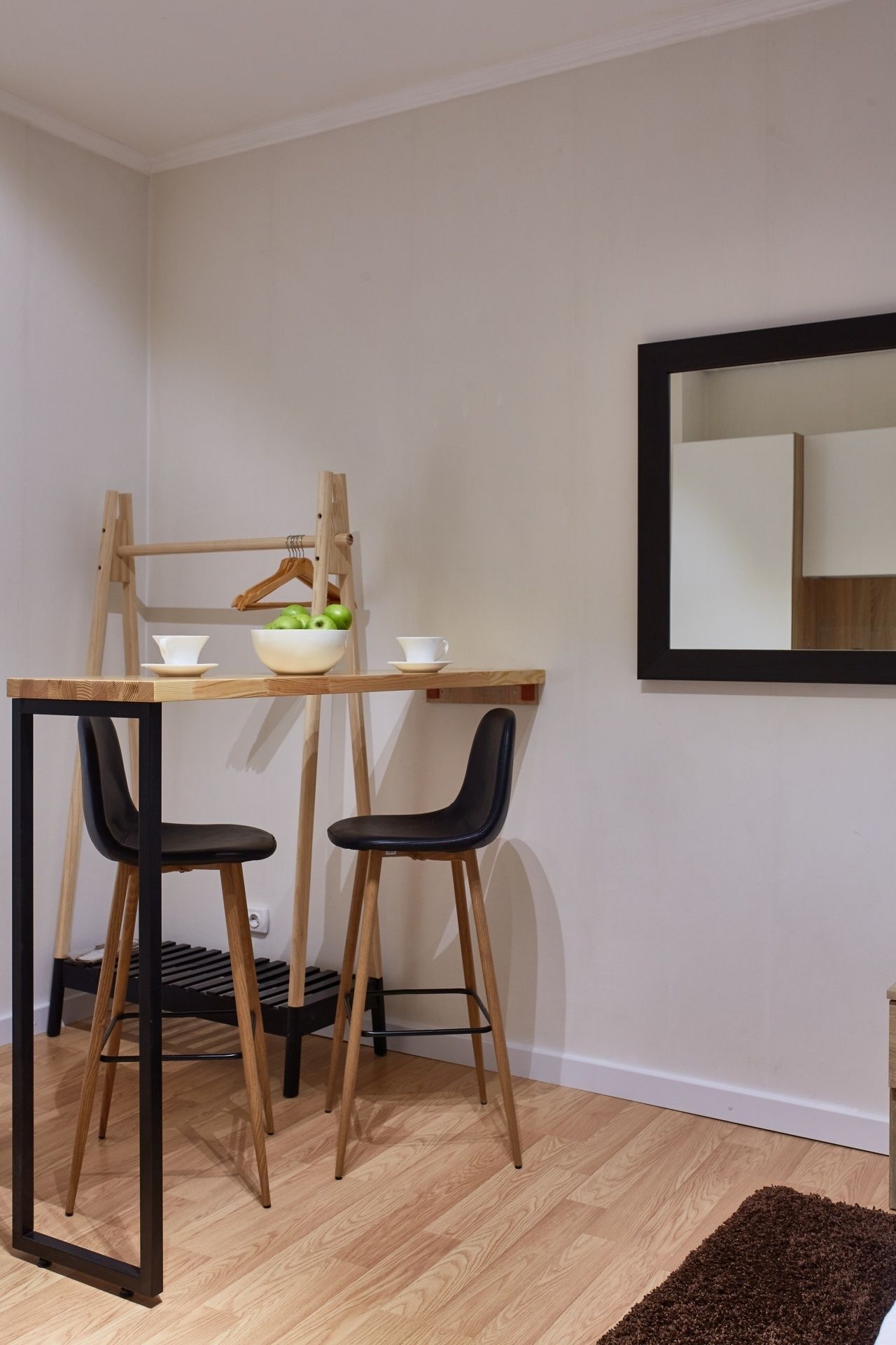 A small, modern room with a wooden table and two black chairs, a wooden ladder, and a mirror on the wall.