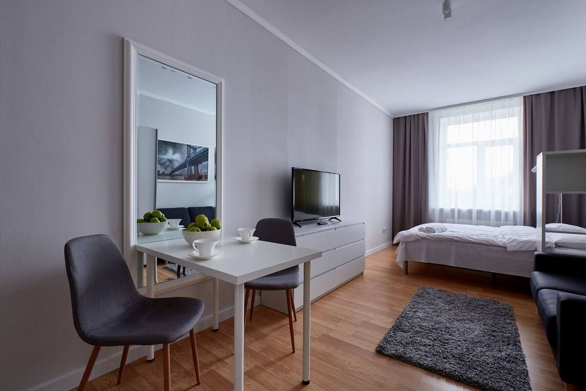 A modern hotel room with a desk, chair, TV, bed, and a large mirror.