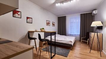 A modern hotel room with a bed, desk, chairs, and a lamp.
