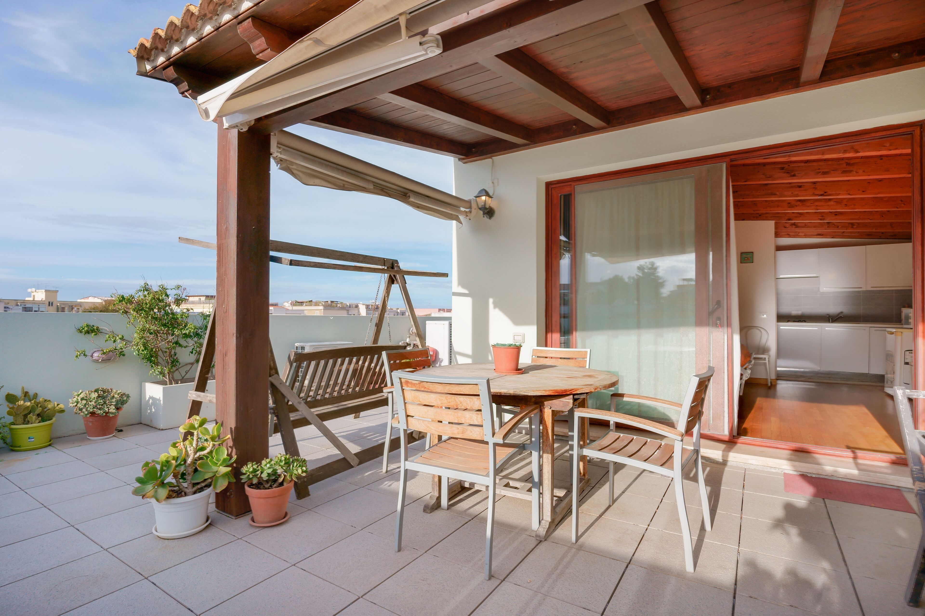 Een balkon met een houten tafel en stoelen, potplanten en uitzicht op de stad.