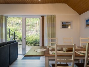 A dining area with a wooden table, white chairs, and a view of a forest through glass doors. - Eifelnatur (Haus 2) by Interhome (Immerath)