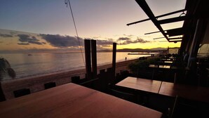 Een restaurant met uitzicht op het strand en de zonsondergang.