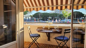 Een terras met een gestreepte luifel, houten tafels en blauwe stoelen met kussens.