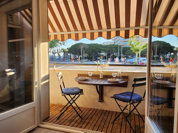 An outdoor dining area with a striped awning, wooden tables, and blue cushioned chairs.