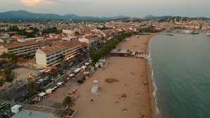 Een kuststadsgezicht met een breed strand, een boulevard met winkels en restaurants, en een bergachtige achtergrond.