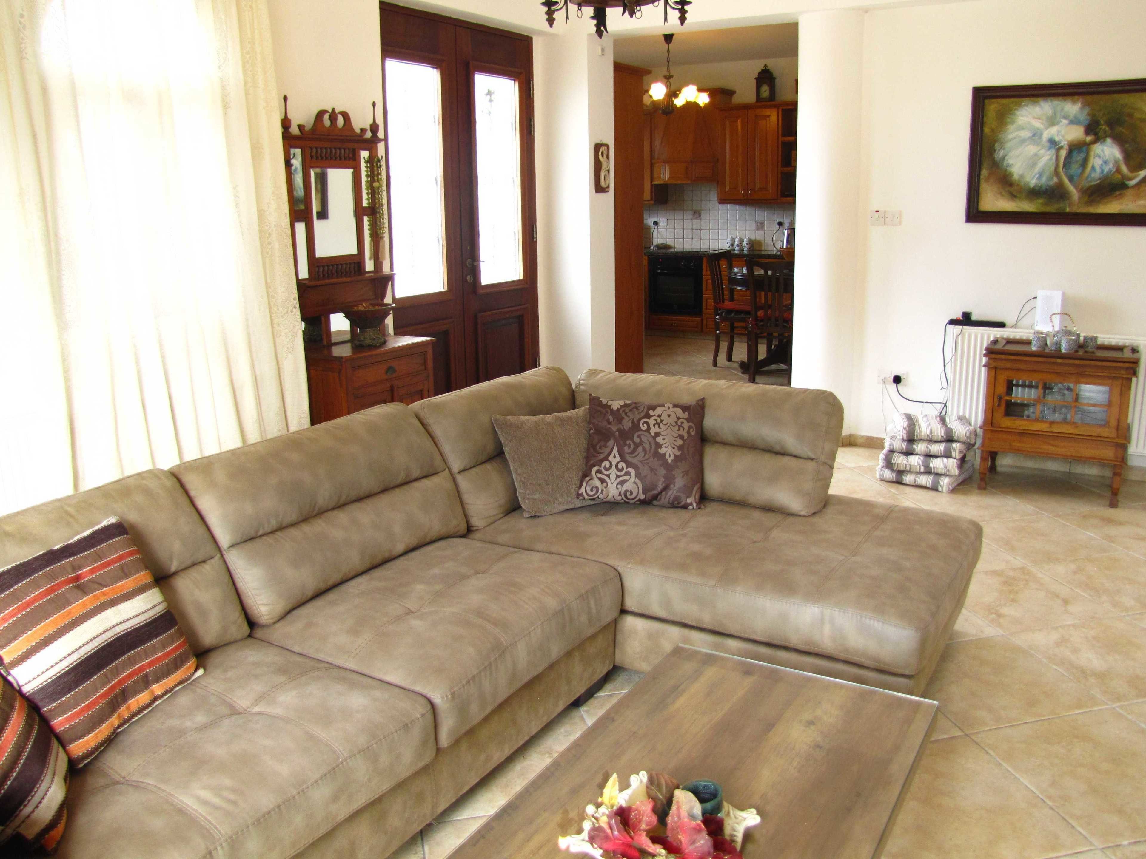 A living room with a beige sectional sofa, a coffee table, and a dining area in the background.