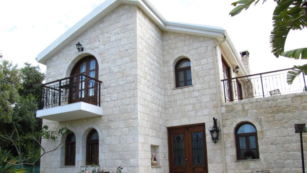 Un edificio de piedra con un balcón, una puerta de madera y un pequeño jardín.