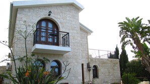 Un edificio de piedra con balcón, ventanas de arco y un jardín con plantas tropicales.