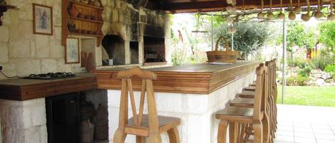 A rustic kitchen with a stone wall, wooden bar stools, and a hanging light fixture.
