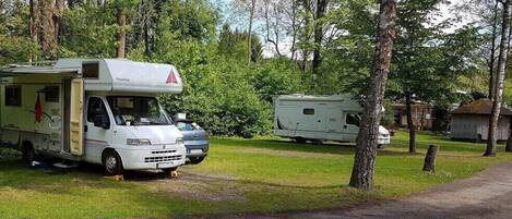 A campsite with two RVs parked on a grassy area surrounded by trees.