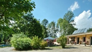 A building with a solar panel roof, surrounded by trees and a gravel area. - Campinghotel Eulenburg - Hostel (Osterode am Harz)