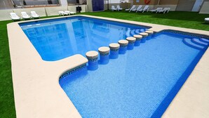 Une piscine au design original, entourée de chaises longues blanches et d’une pelouse verdoyante.
