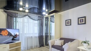 Ein Wohnzimmer mit Fernseher, einer Couch, einem Blumentopf und einer Glasschiebetür, die auf einen Balkon führt.