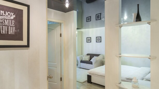 Ein Hotelzimmer mit Bett, einer Couch und einem Regal mit Dekoration. Eine Tür führt in einen weiteren Raum.