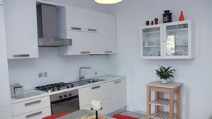 A compact kitchen with white cabinets, a gas stove, and a sink. There's a small table with a candle and a painting. A wooden shelf with a plant is against the wall. - Ca' Lou al Teatro (Vicenza)