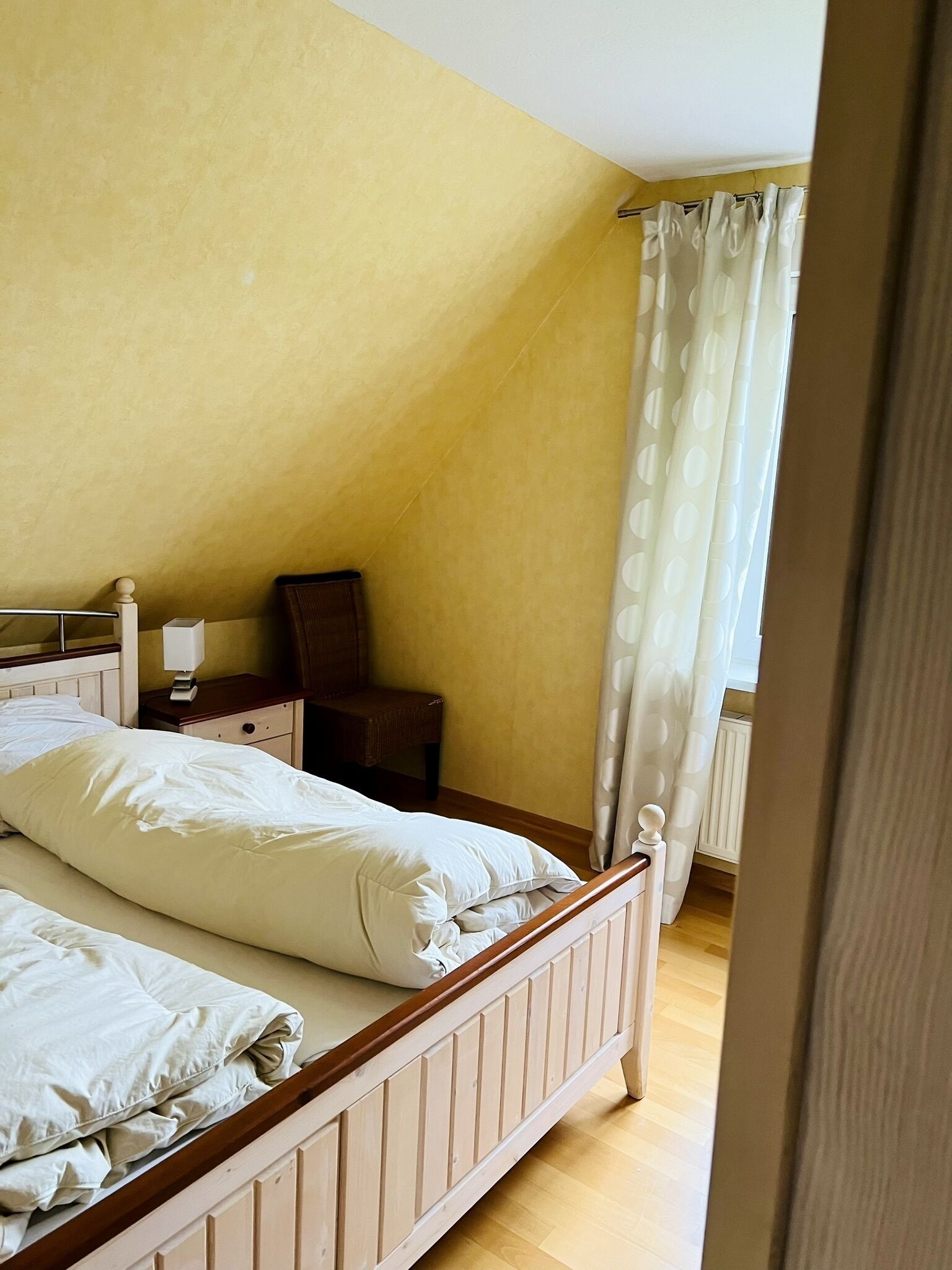 Un dormitorio con una cama de madera, una mesita de noche, una silla y una ventana con cortina.