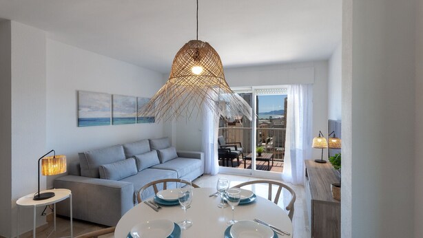 Un espace repas moderne avec une table ronde pour quatre personnes, un canapé gris et une grande fenêtre donnant sur la ville.