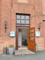 Ein Backsteinhaus mit einem Holzeingang, einem Schild mit der Aufschrift 'Hotel Eingang' und zwei Wandleuchten.