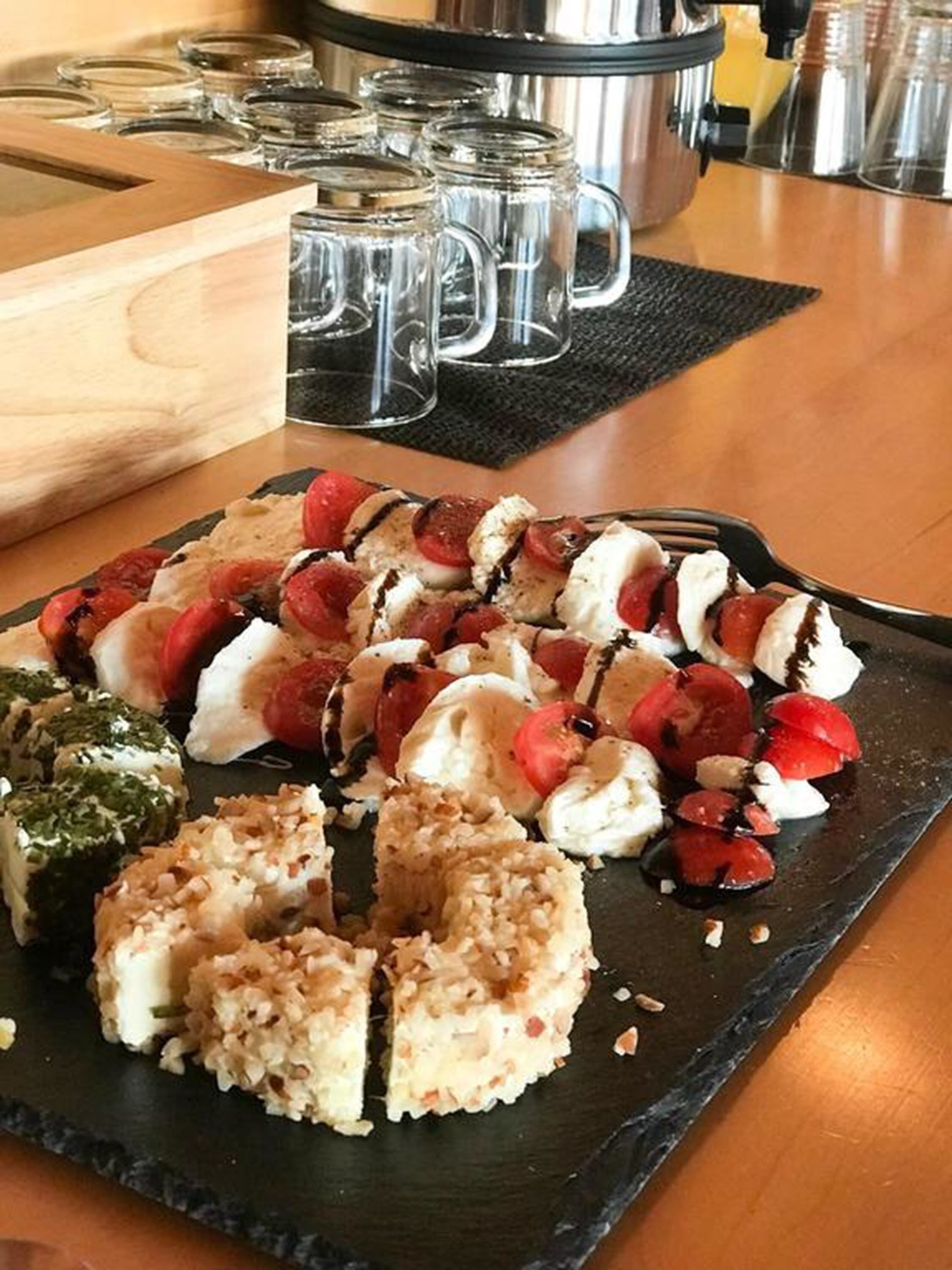 Verschiedene Sushi- und Sashimi-Sorten auf einer Schieferplatte, mit Schneidebrett aus Holz und Glasbechern im Hintergrund.