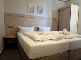 Ein Hotelzimmer mit zwei Betten, einem Holzkopfstück, weißen Leinentüchern und zwei an der Wand befestigten Kunstwerken.