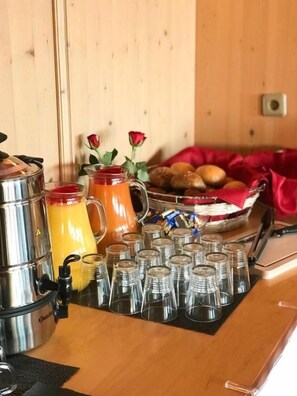 A breakfast buffet setup with a coffee maker, a pitcher of orange juice, and a bowl of fruit.
