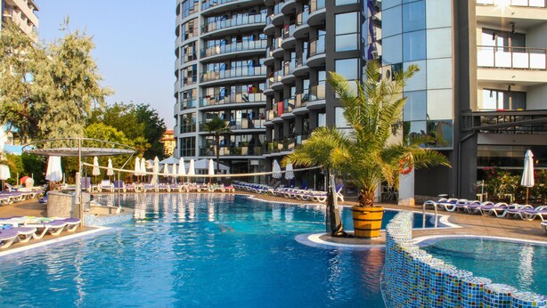 A swimming pool with lounge chairs and umbrellas, surrounded by a modern building with balconies. - Smartline Meridian Hotel (Sunny Beach)
