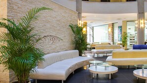A modern lobby with a stone wall, white sofas, and glass tables. - Smartline Meridian Hotel (Sunny Beach)