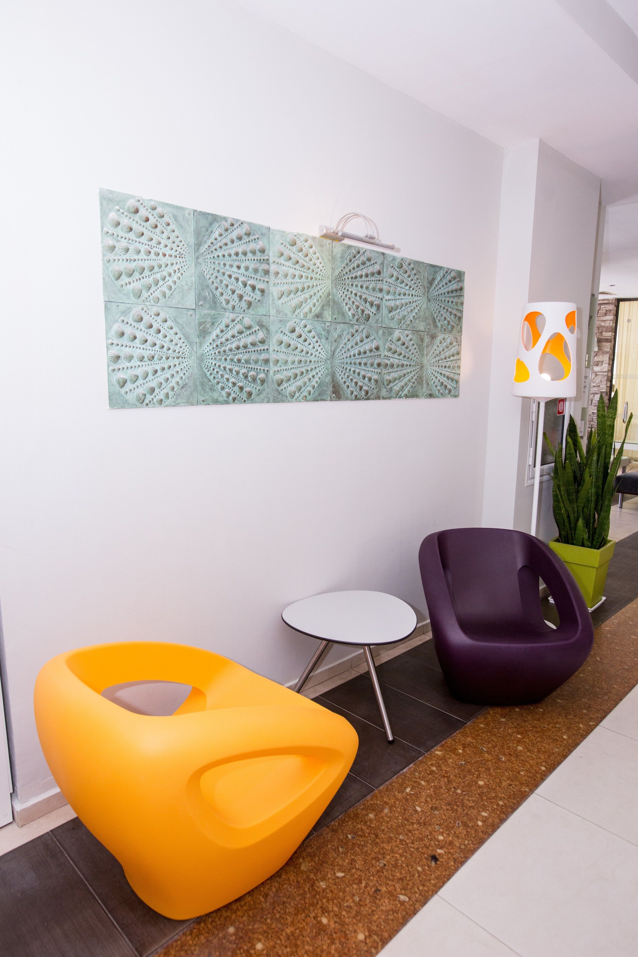 A modern lobby with a geometric wall art, a small round table, and colorful chairs.