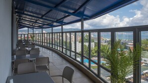 A covered outdoor seating area with tables and chairs, large windows offering a view of the city and water. - Smartline Meridian Hotel (Sunny Beach)