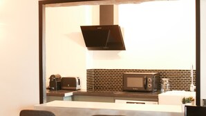 A modern kitchen with a black microwave, toaster, and coffee maker on the counter. There are two blue bar stools and a small table with a TV. - House Alberta Superb T2 in the city center (Aix-en-Provence)