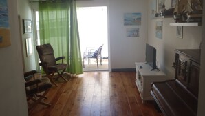 A living room with wooden flooring, a green curtain, a rocking chair, a TV stand, and a piano. - --- SEA AND BOATS ---- (Le Portel)