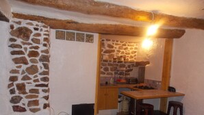A compact kitchen with stone walls, wooden beams, a small table, stools, and basic appliances. - Nice little studio 20 M2 (AUPS)