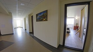 Ein langer, schmaler Flur mit einem Bild an der Wand, der zu einem Zimmer mit einem Bett und einem kleinen Tisch führt.