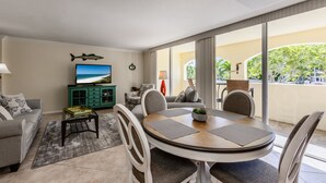 Ein modernes Wohnzimmer mit einem runden Esstisch, bequemen Sitzgelegenheiten, einem Fernseher und Blick ins Freie.
