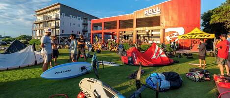 A building with a 'REAL' sign, a grassy area with surfboards, and tents.