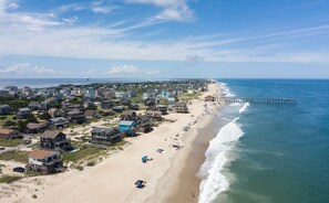 A coastal town with beachfront properties, a pier extending into the ocean, and a clear sky.