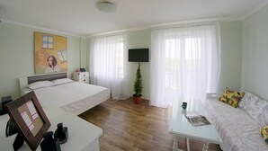 A hotel room with a bed, a desk, a chair, a small table, a TV, and a potted plant. - Flatsis Apartment Otakara Yarosha 33 (Kharkiv)