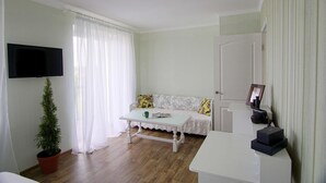 A room with a white sofa, a small table, a potted plant, a flat-screen TV, and a door with a mirror. - Flatsis Apartment Otakara Yarosha 33 (Kharkiv)