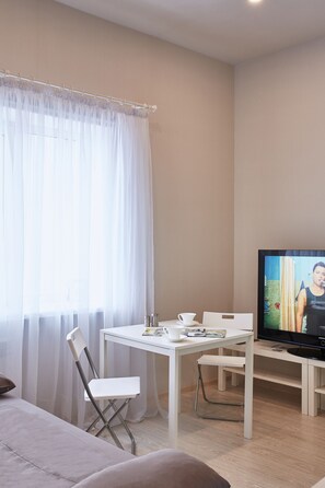 A modern room with a white table, a TV, a white chair, and a sofa.