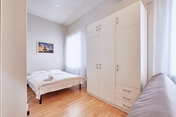 A bedroom with a bed, a wardrobe, and a painting of the Eiffel Tower.