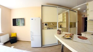 Een ruimtelijke zithoek met een kitchenette, een koelkast, een bed en een eethoek.