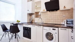 Een moderne keuken met een ingebouwde vaatwasser, wasmachine en een magnetron. Er staan twee zwarte stoelen en er is een raam dat voor natuurlijk licht zorgt.