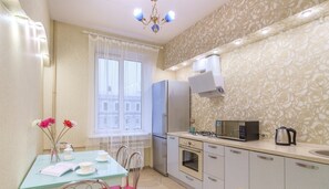 A compact kitchen with a refrigerator, microwave, stove, and kettle. There is a dining table with chairs and a vase of flowers. - Flatsis Apartment Konstitutsii 2 (Kharkiv)