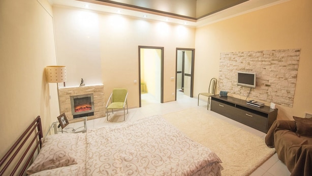 A bedroom with a bed, a fireplace, a TV mounted on a stone wall, and a desk with a chair. - Flatsis Apartment Kuznechnaya 13 (Kharkiv)