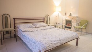 A neatly arranged bedroom with a bed, two chairs, a table, and a fireplace. - Flatsis Apartment Kuznechnaya 13 (Kharkiv)