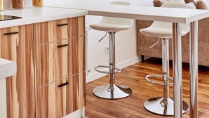 Eine moderne Küche mit Holzschränken, weißen Arbeitsplatten und Barhocker aus Edelstahl.