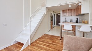 Eine moderne Wohnung mit einer Holztreppe, einer Küche mit weißen Schränken und einem Essbereich mit weißem Tisch und Stühlen.