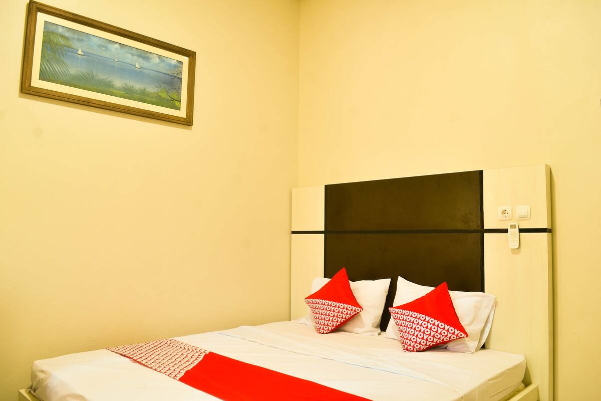 Ein Hotelzimmer mit einem Bett, einem Bild an der Wand und einem roten und weißen Kopfkissen.