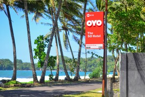 Une enseigne pour l’hôtel OYO The SO, avec en arrière-plan des palmiers et une plage.